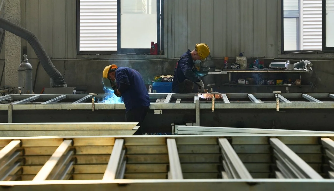 Workers welding steel chassis frames for expandable homes in a manufacturing facility