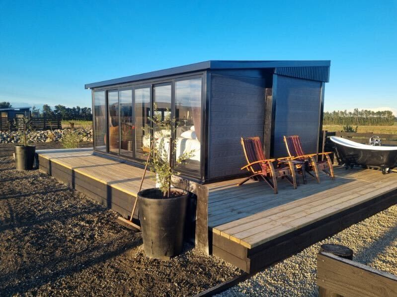 A black-clad tiny home with deck, outdoor bath and evening light
