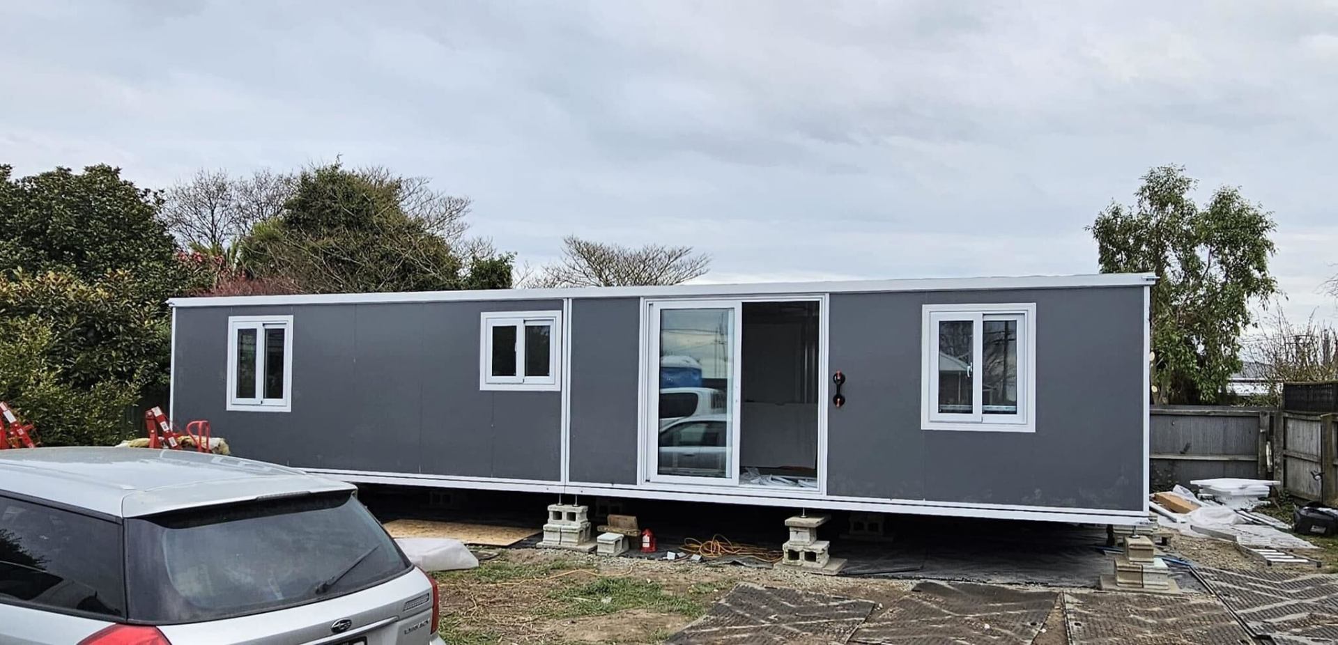 A grey portable tiny home newly delivered onto a Kiwi section