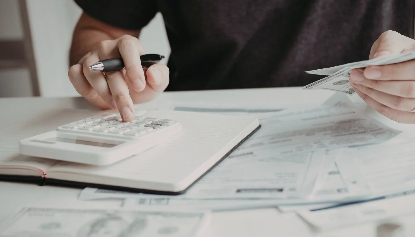 Hands using a calculator and counting cash while reviewing building cost paperwork